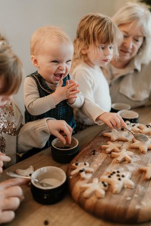 Family baking together at wooden table with cookies and dough while laughing and having fun.