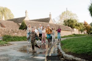 A group of people walking together on a grassy path during a sunny autumn day near stone buildings.