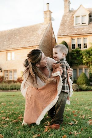 A heartwarming autumn scene shows playful interaction between parent and child on a grassy lawn near stone buildings.