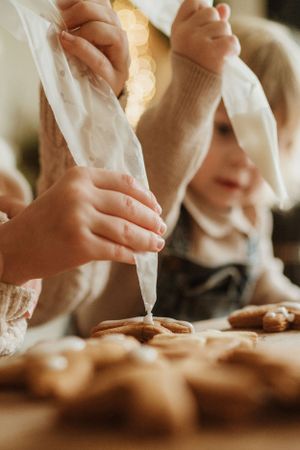 Close-up shot of hands piping frosting onto freshly baked cookies during holiday baking.