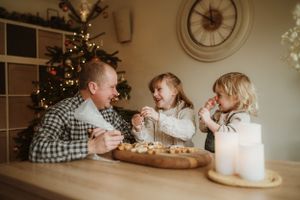 Cozy indoor family scene with Christmas tree and wall clock visible in background.