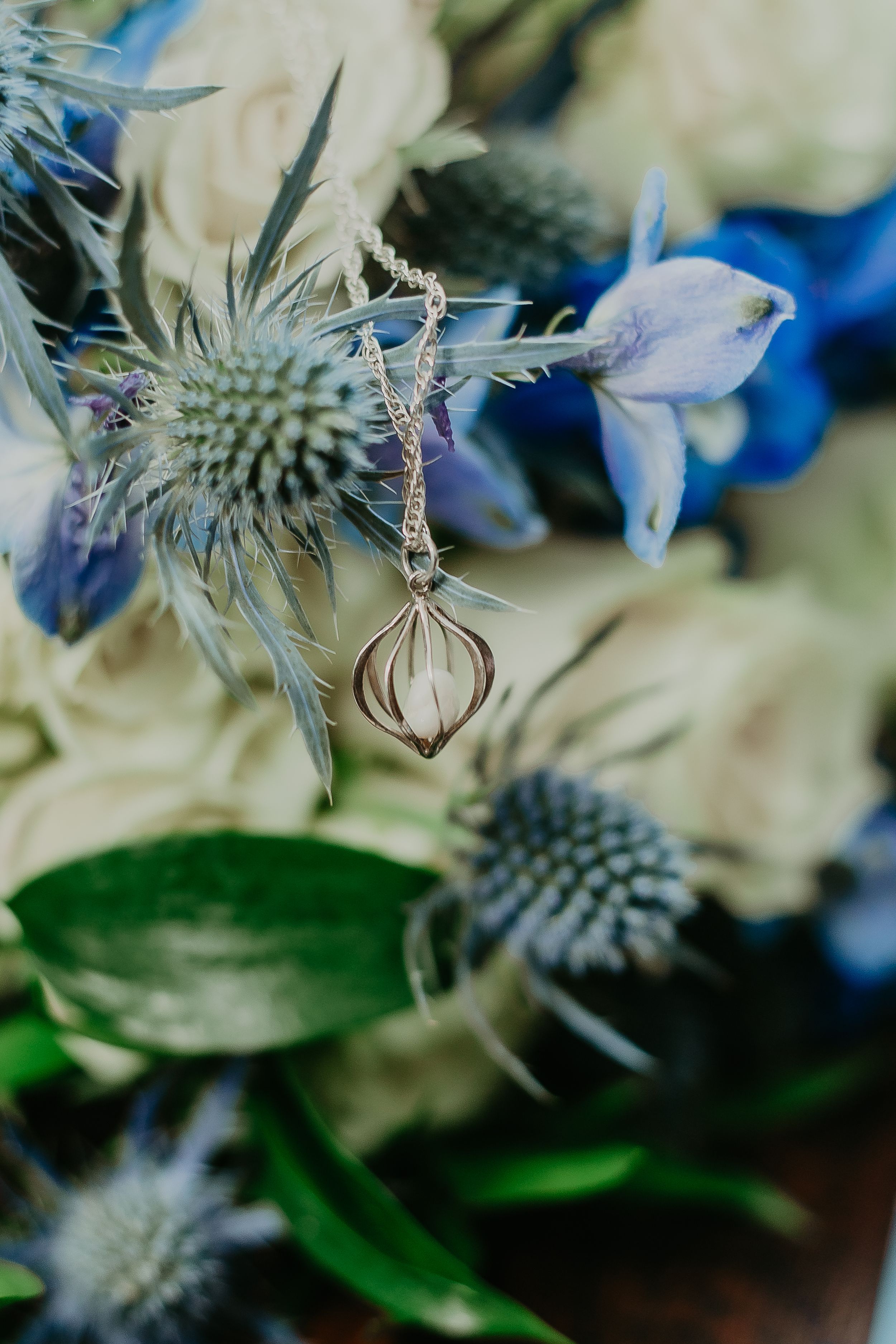 Delicate gold pendant necklace draped over a blue and white bridal bouquet.