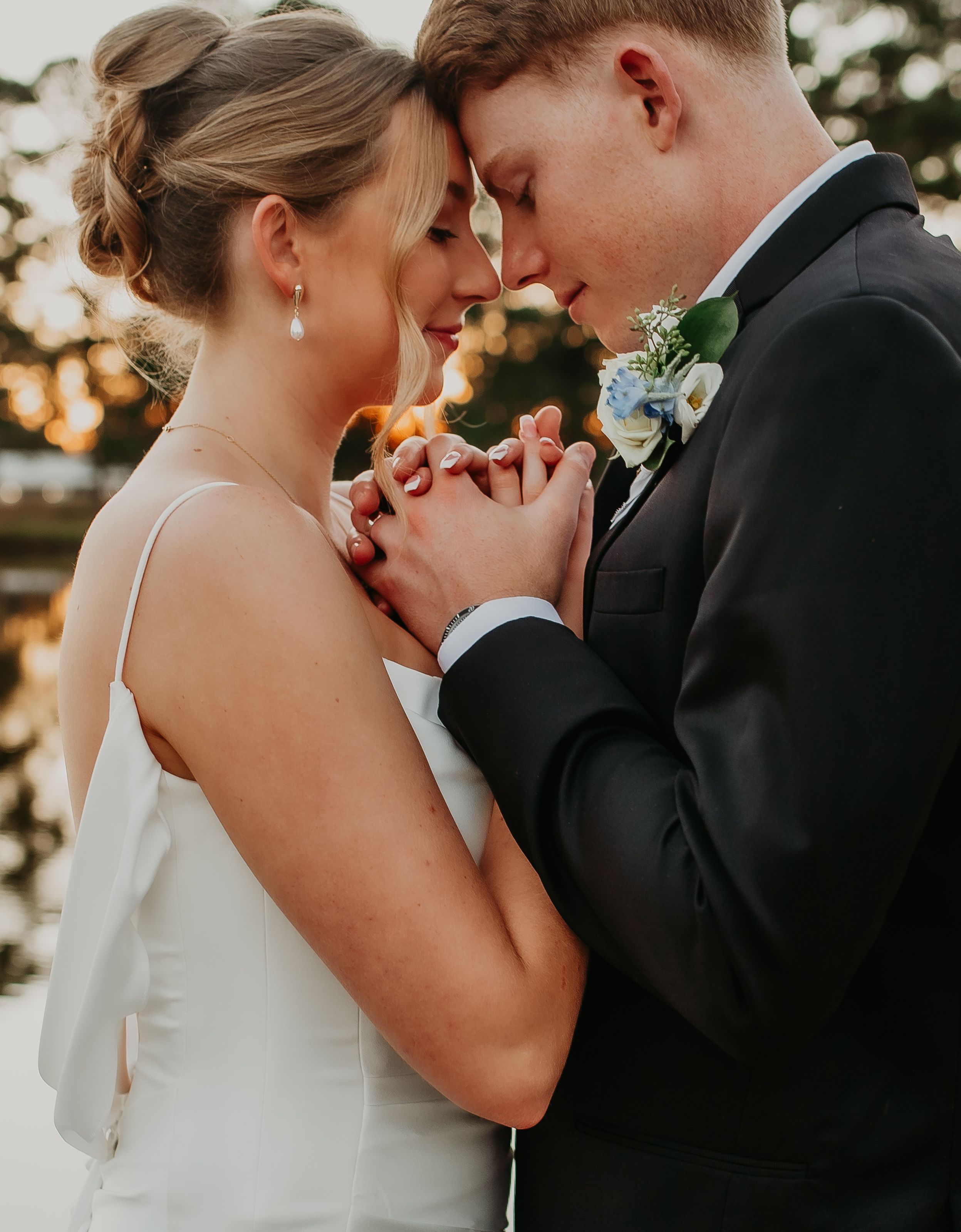 Bride and groom tenderly hold hands and touch foreheads in an intimate wedding portrait.