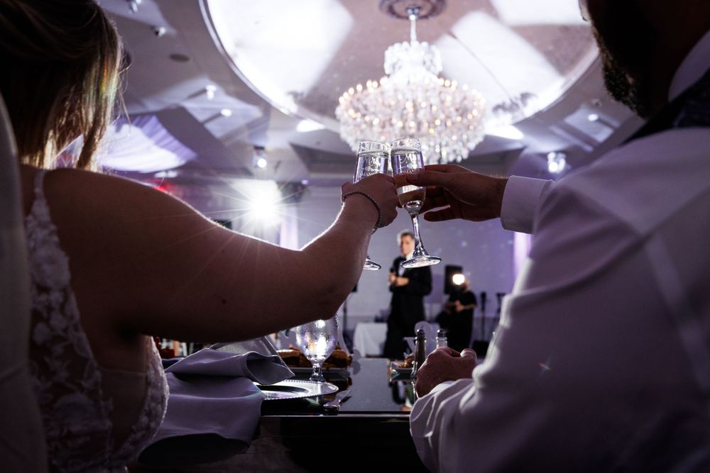 Bride and groom toasting with champagne glasses under a crystal chandelier at their wedding reception.