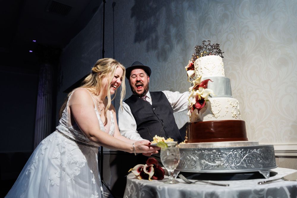 Joyful bride and groom laughing while cutting their elegant multi-tiered wedding cake at their reception.