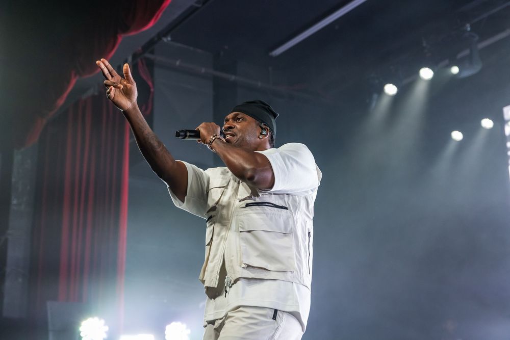 A performer in a white shirt energetically dances and sings on stage during a concert performance.
