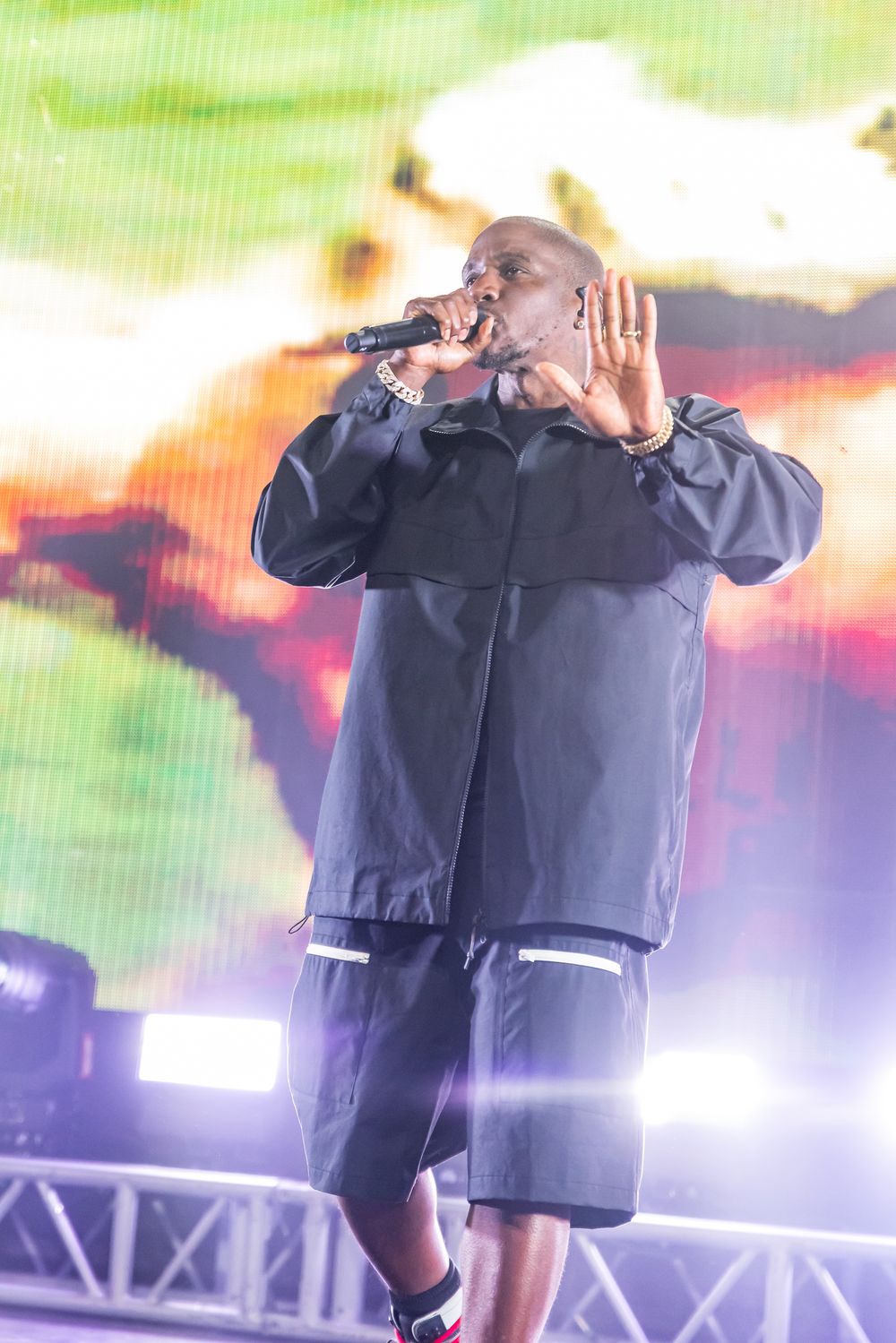 A performer in a navy blue outfit energetically sings on stage with dramatic lighting effects in the background.