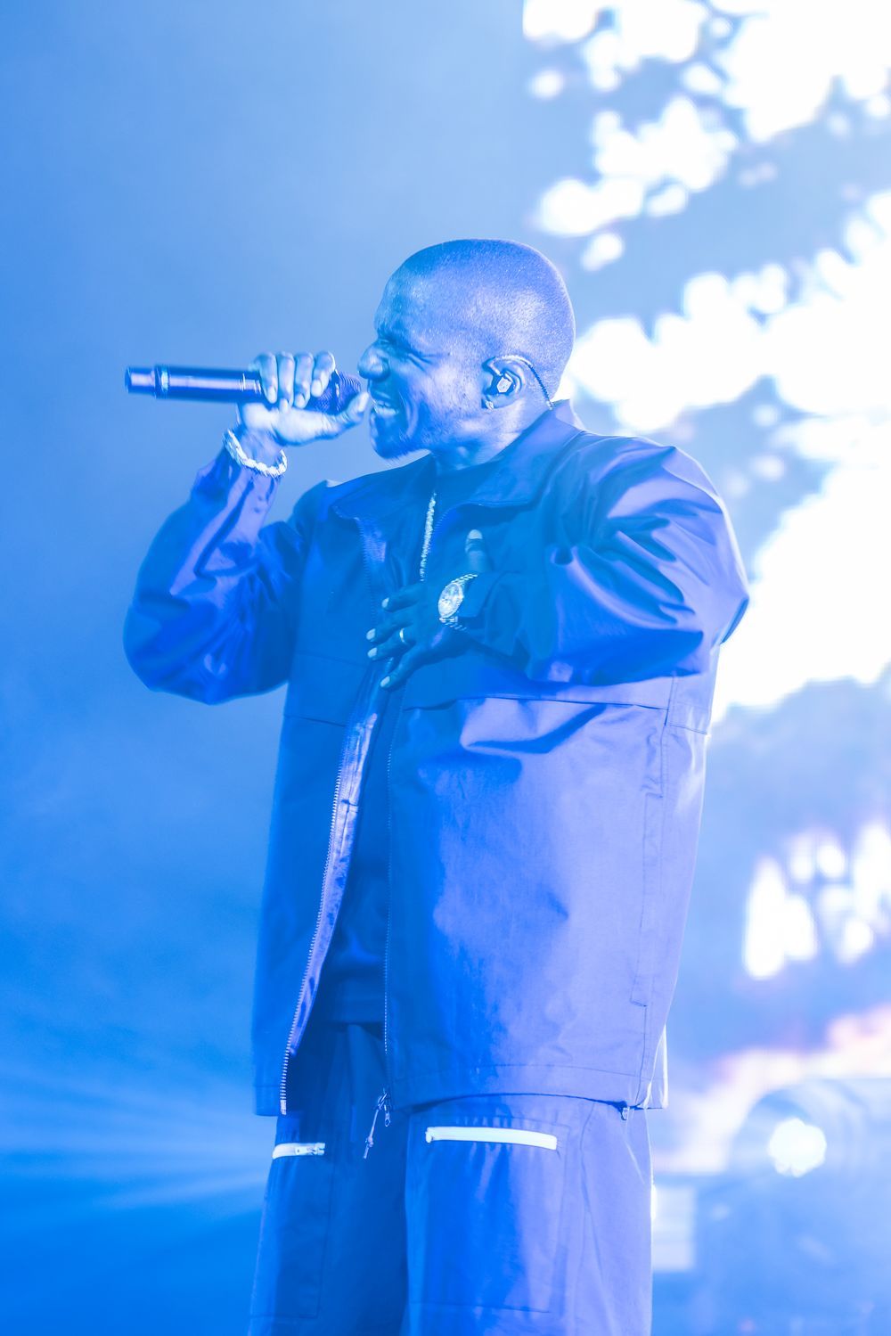 A performer in dark clothing is silhouetted against a blue-lit stage background during a live concert performance.