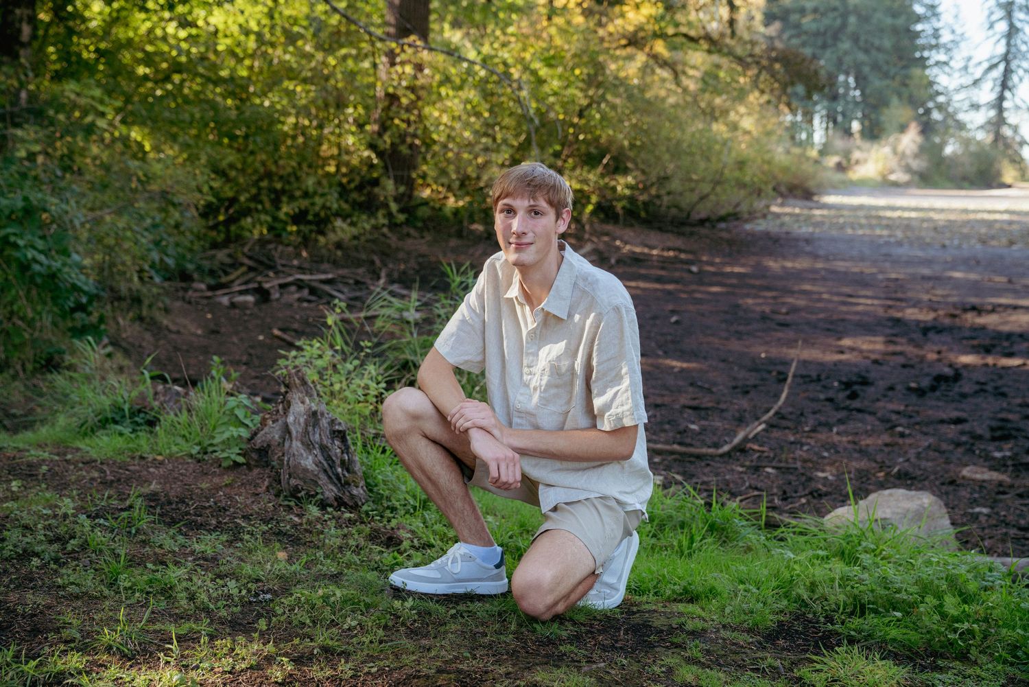 Senior boy crouching on forest path, casual outdoor senior portraits in Oregon, PNW greenery.
