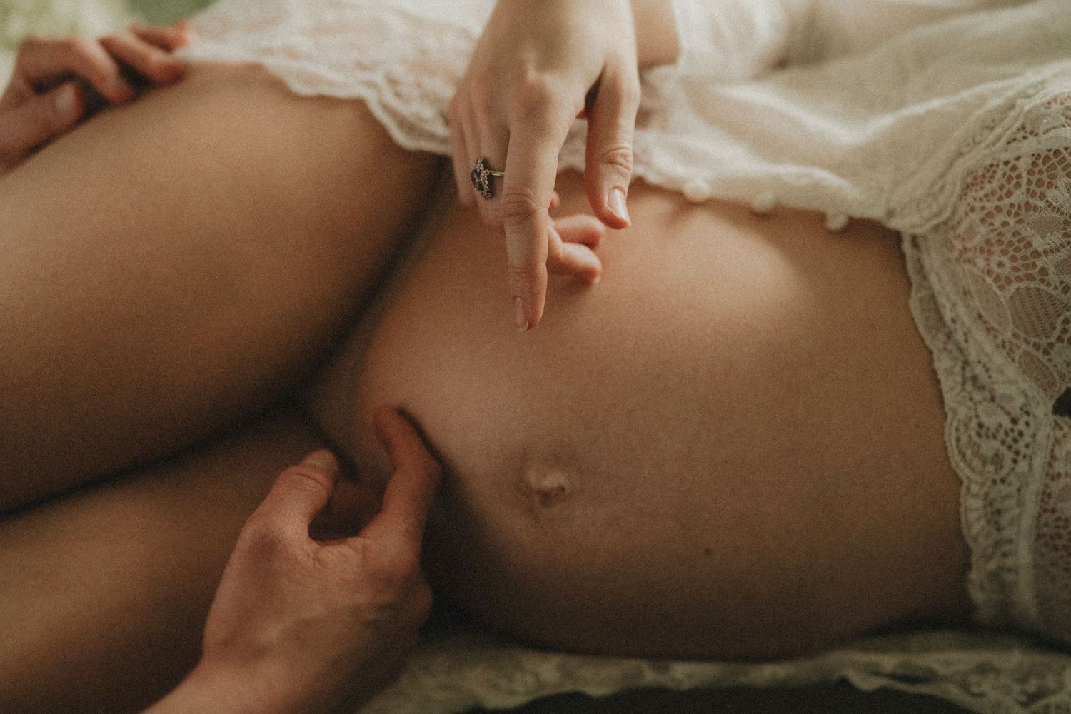 Intimate couple moment captured on white bedding in soft natural light during maternity session by pausing time photography Cheltenham