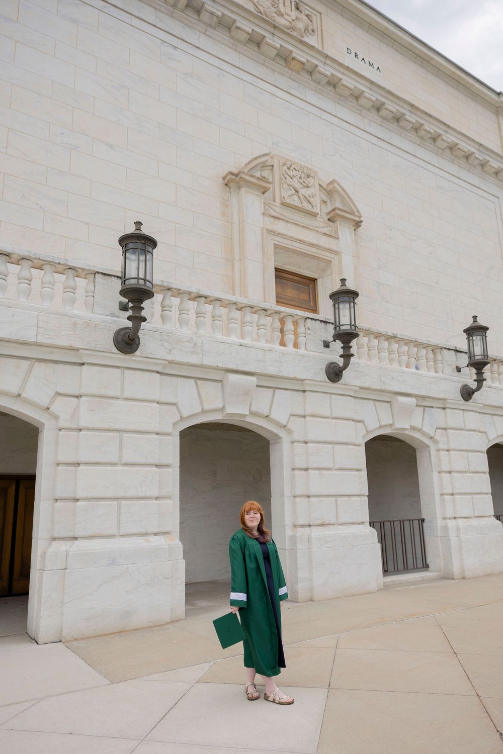 Graduate in green cap and gown posing outside a grand white stone building with ornate architecture at DIA in Detroit michigan