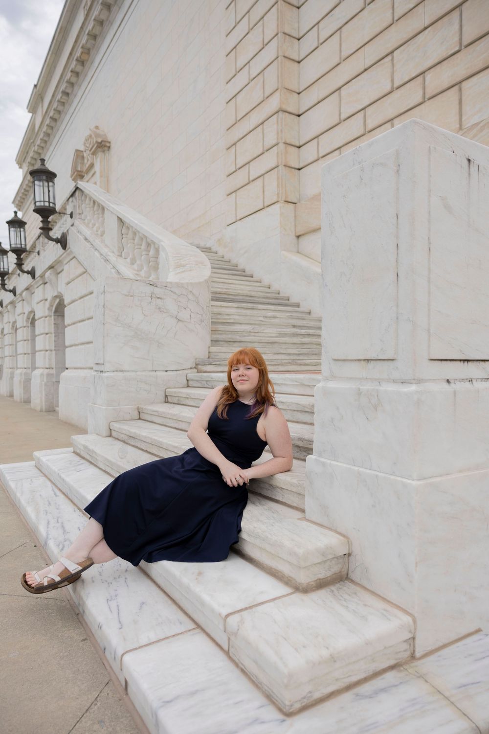 Woman in navy dress sitting on marble steps of a grand art building with ornate architecture at Detroit institute of arts for senior photos