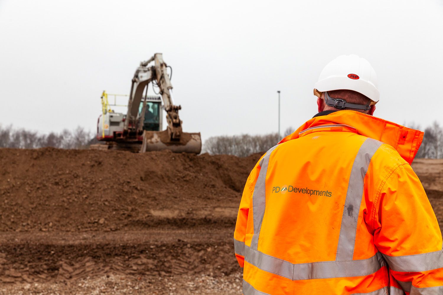 Construction photograph of foreman watching digger on building site