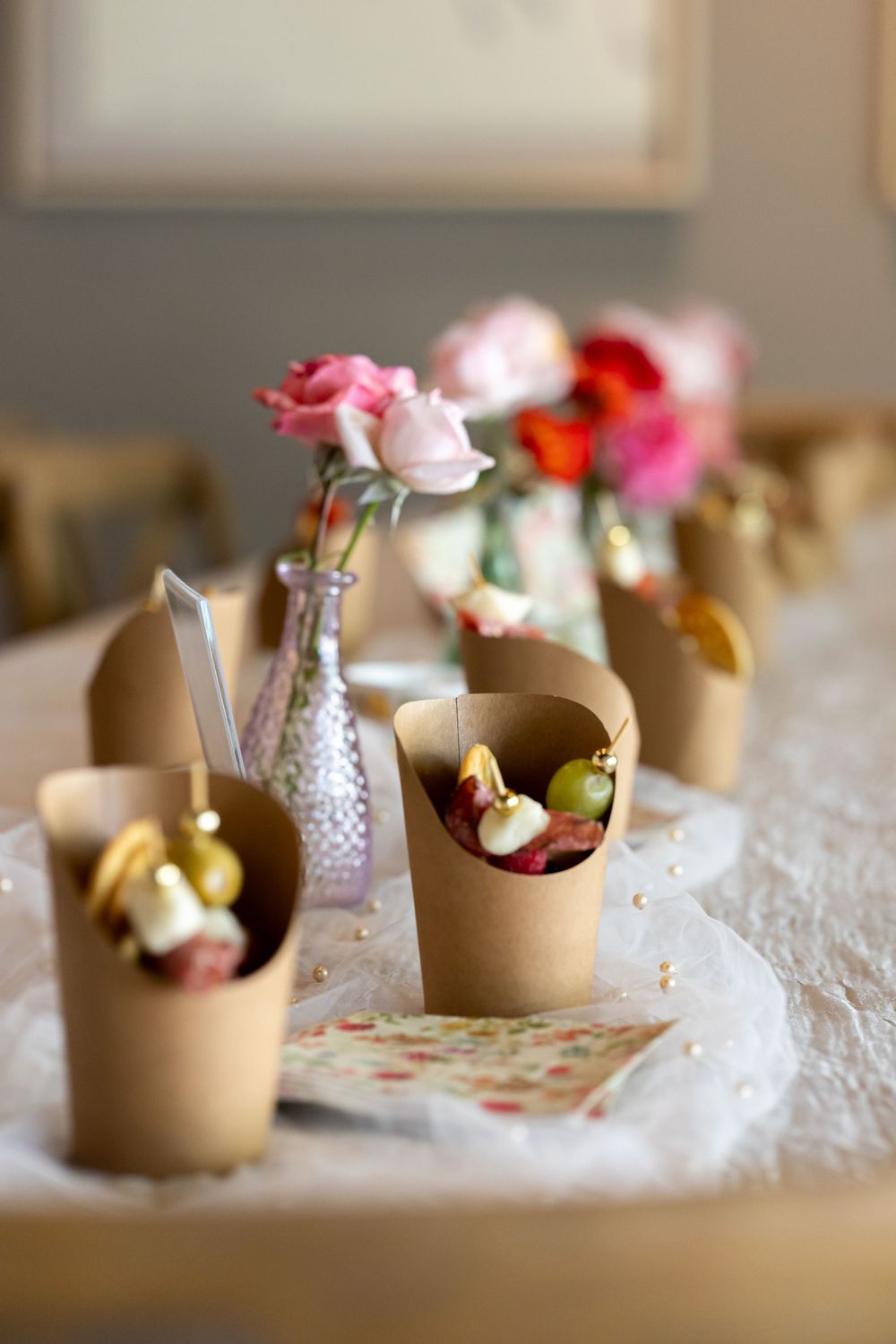 Table setting with kraft paper cones and pink roses in vintage vase.