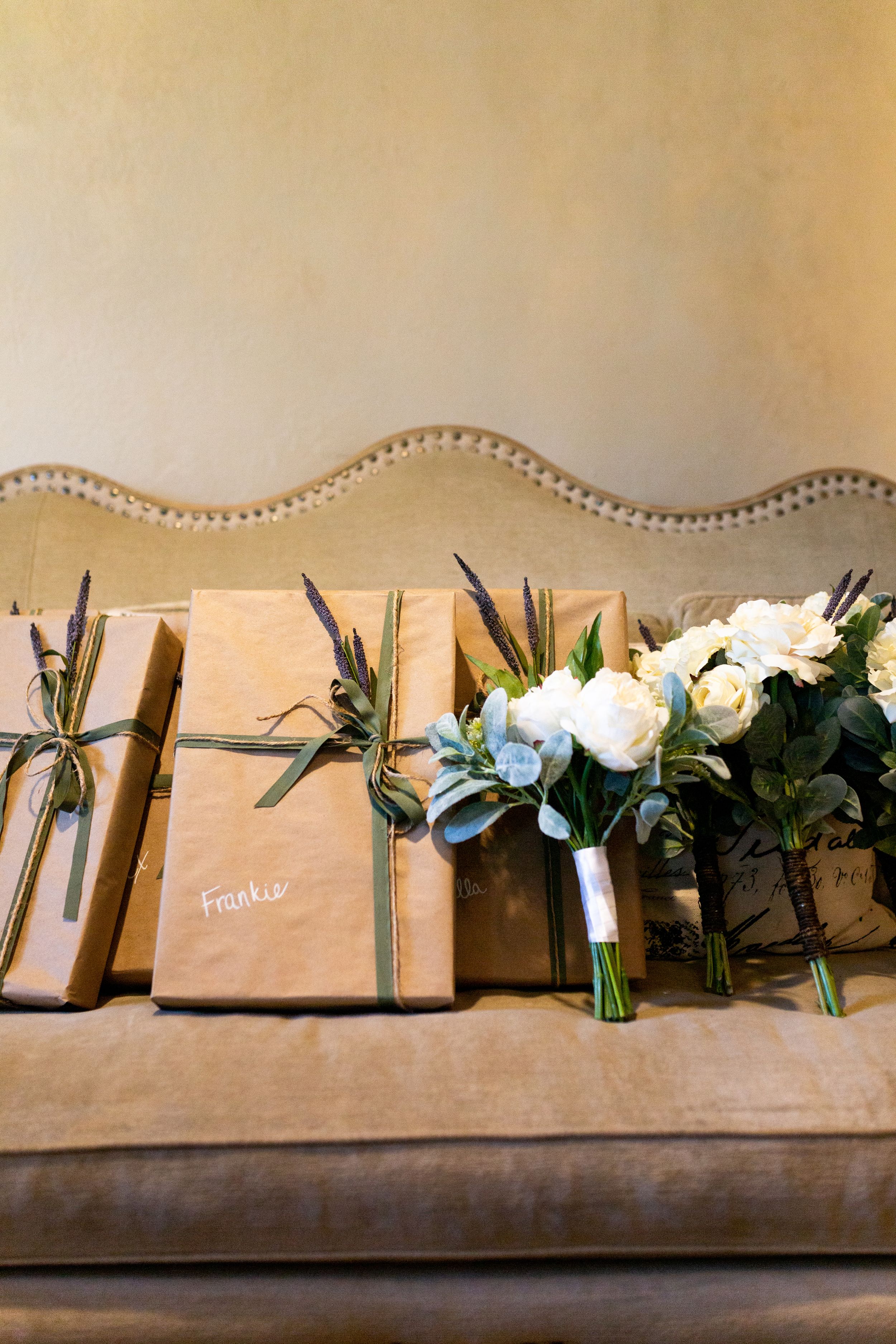 Wedding bouquets and brown paper packages with name tags arranged on an upholstered bench.