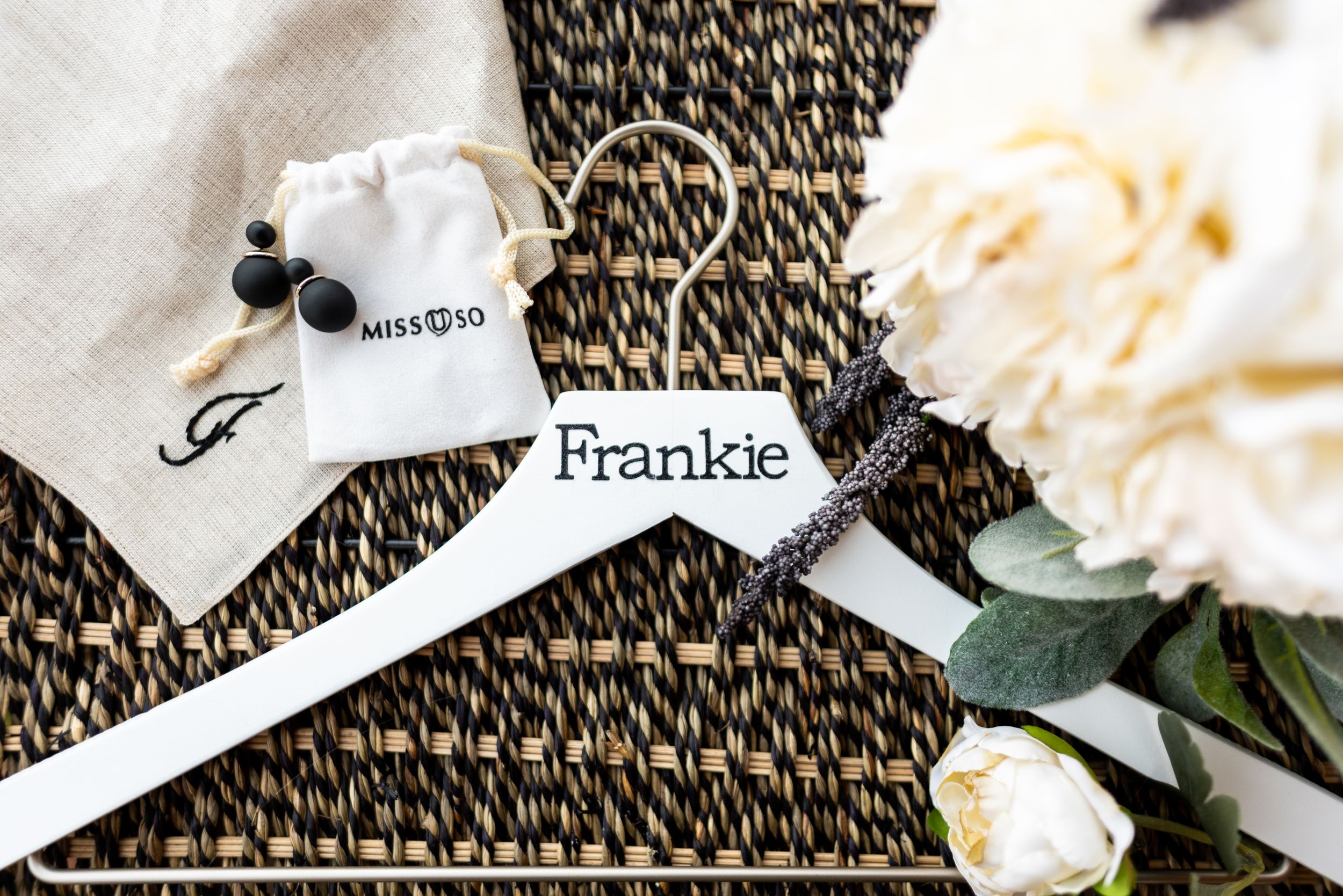 Wedding detail photo showing personalized name tags and a white rose on a textured mat background.