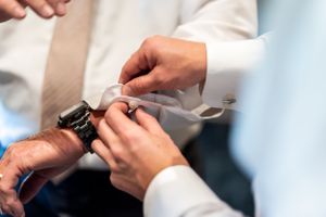 Close-up of hands adjusting cufflinks on a white dress shirt sleeve.