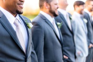 Row of groomsmen in grey suits with boutonnieres standing in formal lineup.