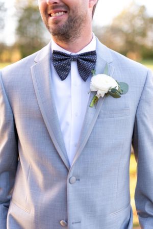 Close-up of grey suit jacket with polka dot bowtie and white rose boutonniere.