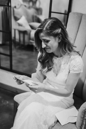 A bride in a lace wedding dress sits looking at her phone.