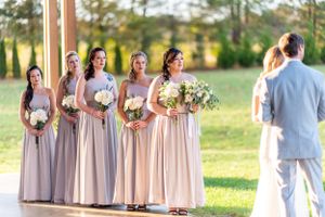 Bridesmaids in blush dresses stand in line during outdoor ceremony.
