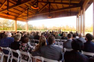 Wedding guests seated under wooden pavilion during sunset ceremony.