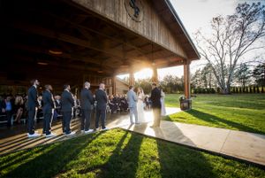 Sunset wedding ceremony under wooden pavilion with dramatic lighting.