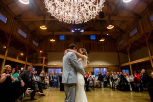 Newlyweds dance under a grand chandelier in a rustic wooden reception hall.