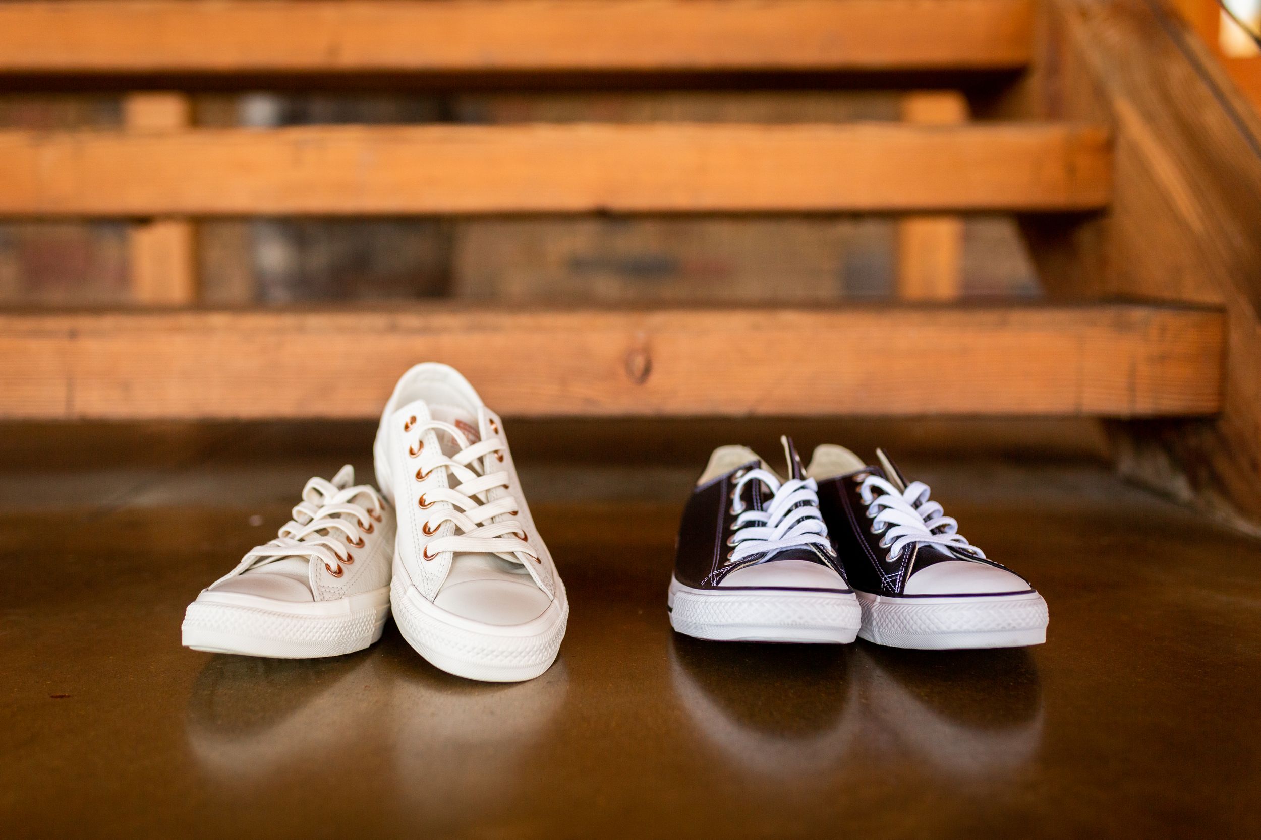 Two pairs of casual sneakers arranged on wooden steps, one white and one black.