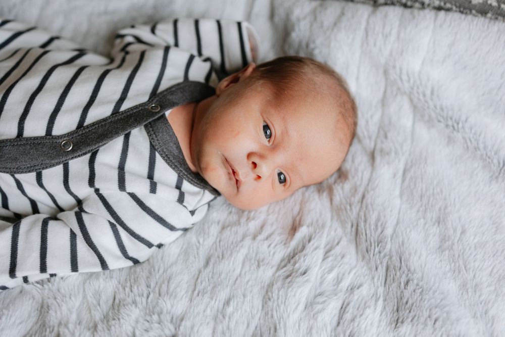 A baby wearing a white and black striped outfit lays on a soft white blanket.