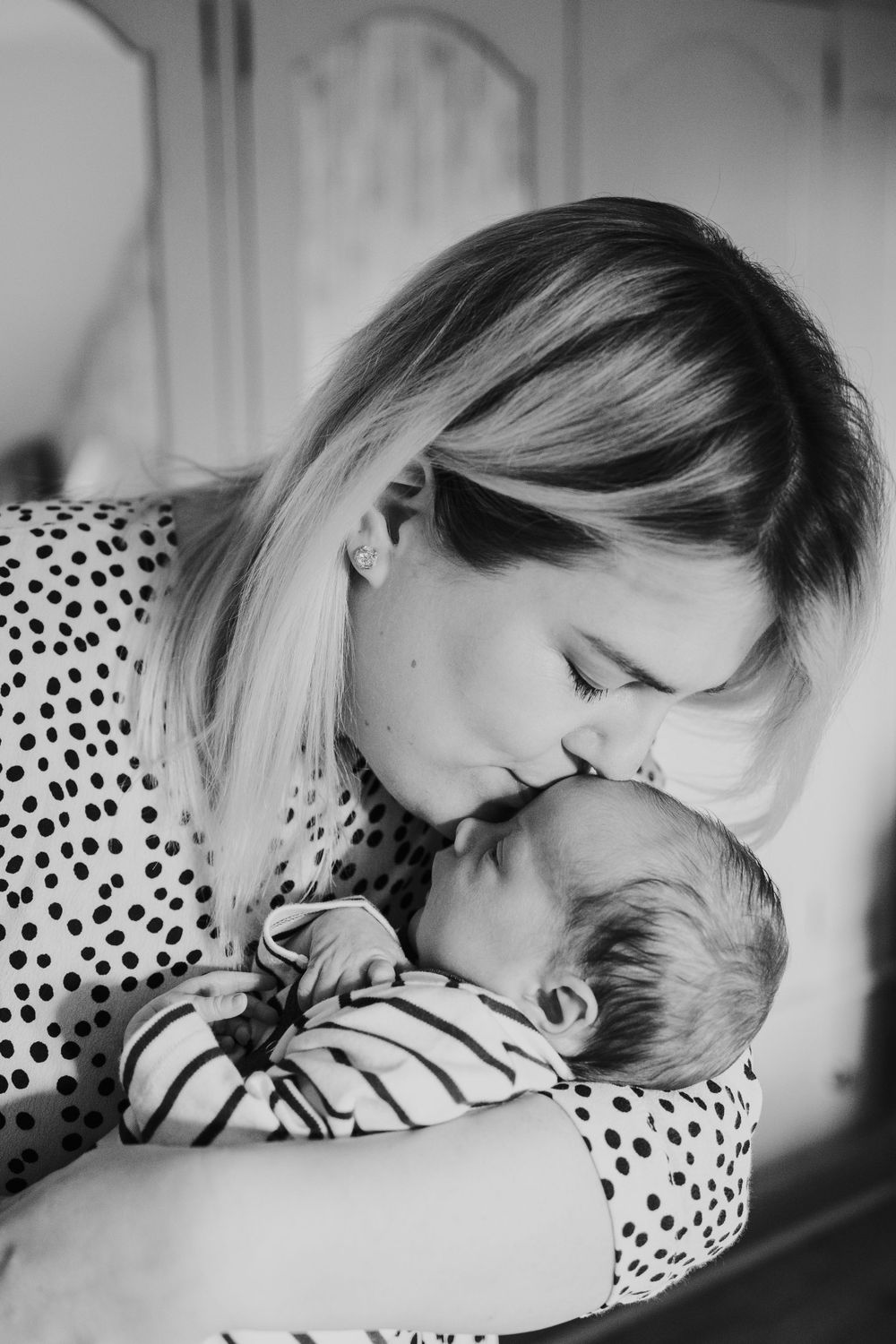A tender black and white moment between parent and baby as they share a gentle embrace while wearing polka dots and stripes.