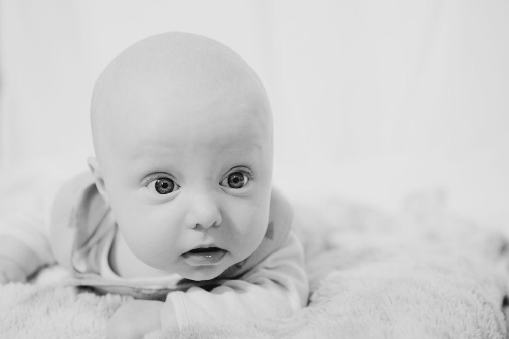Close up black and white portrait of an infant laying on soft fabric with wide-eyed expression.