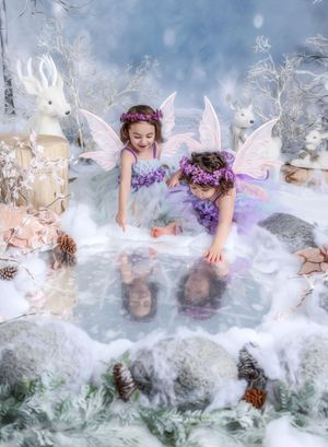 Two young girls dressed as fairies with wings and floral crowns play in a magical winter wonderland scene.