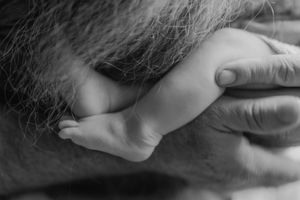 Black and white close-up of a newborn baby's tiny feet held gently in a bearded father's hands.