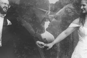 Black and white double exposure wedding photo of bride and groom kissing, surrounded by lush foliage.