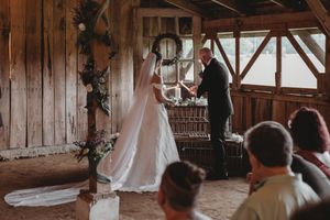 Bride and groom exchange vows in a rustic barn wedding ceremony with wooden walls and floral arch decor.