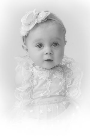 Black and white portrait of a baby girl in lace dress and floral headband, looking at camera.