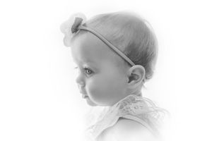 Black and white profile portrait of a baby girl wearing a bow headband and lace dress.