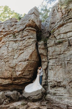 Bride and groom embracing in a dramatic rocky canyon crevice, wedding dress flowing over boulders.