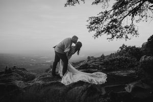 Black and white photo of bride and groom sharing a romantic kiss on rocky overlook with sweeping landscape views.