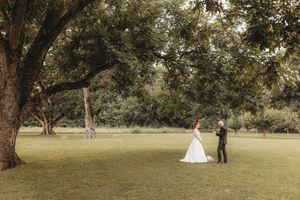 Bride and groom share a romantic first look moment beneath a large oak tree in a lush green garden.