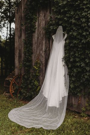 A flowing white bridal veil hangs against a rustic wooden fence surrounded by lush green ivy in an outdoor garden setting.