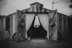 Black and white photo of a rustic barn wedding venue with open doors and elegant white draping.