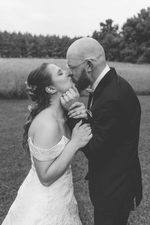 Bride and groom share a tender kiss while holding hands in a black and white outdoor wedding portrait.