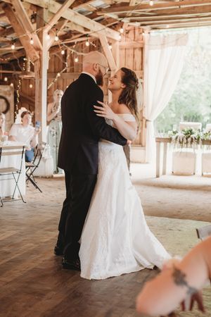 Bride and groom share their first dance in a rustic barn wedding venue adorned with string lights and white curtains.