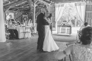 Black and white photo of bride and groom sharing their first dance in a rustic barn wedding venue.