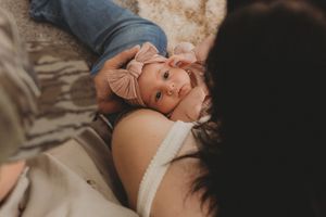Newborn baby with pink bow headband lying on a soft blanket between two parents in a cozy home setting.