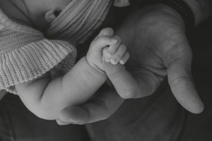 Black and white photo of a newborn baby grasping an adult finger in a tender parent-child bonding moment.