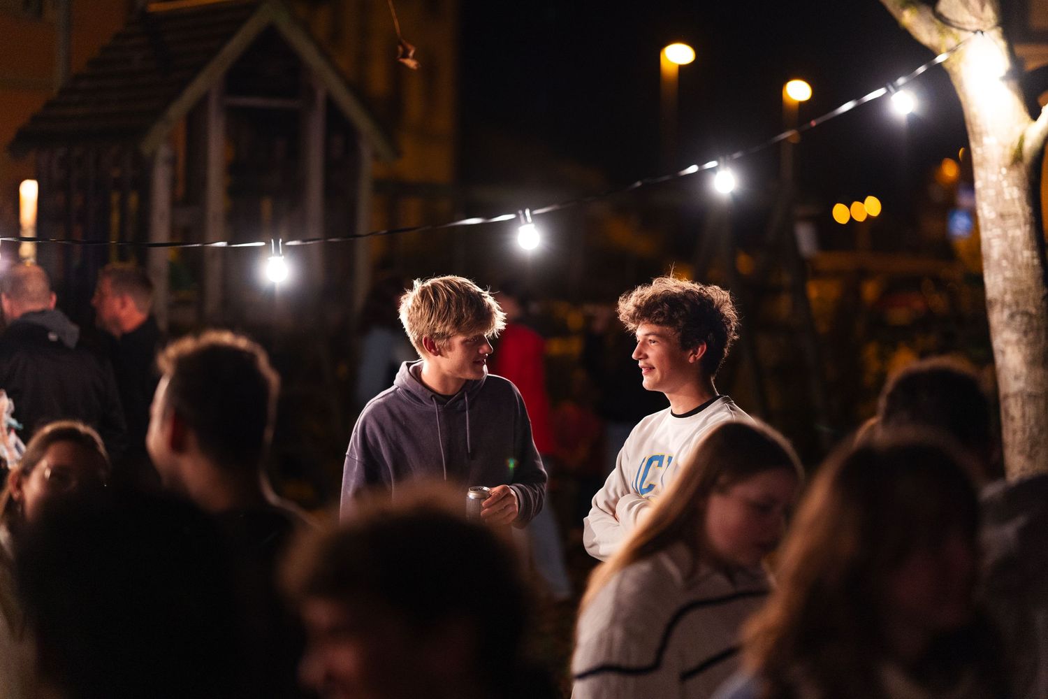Two people chat under string lights at an outdoor nighttime event.