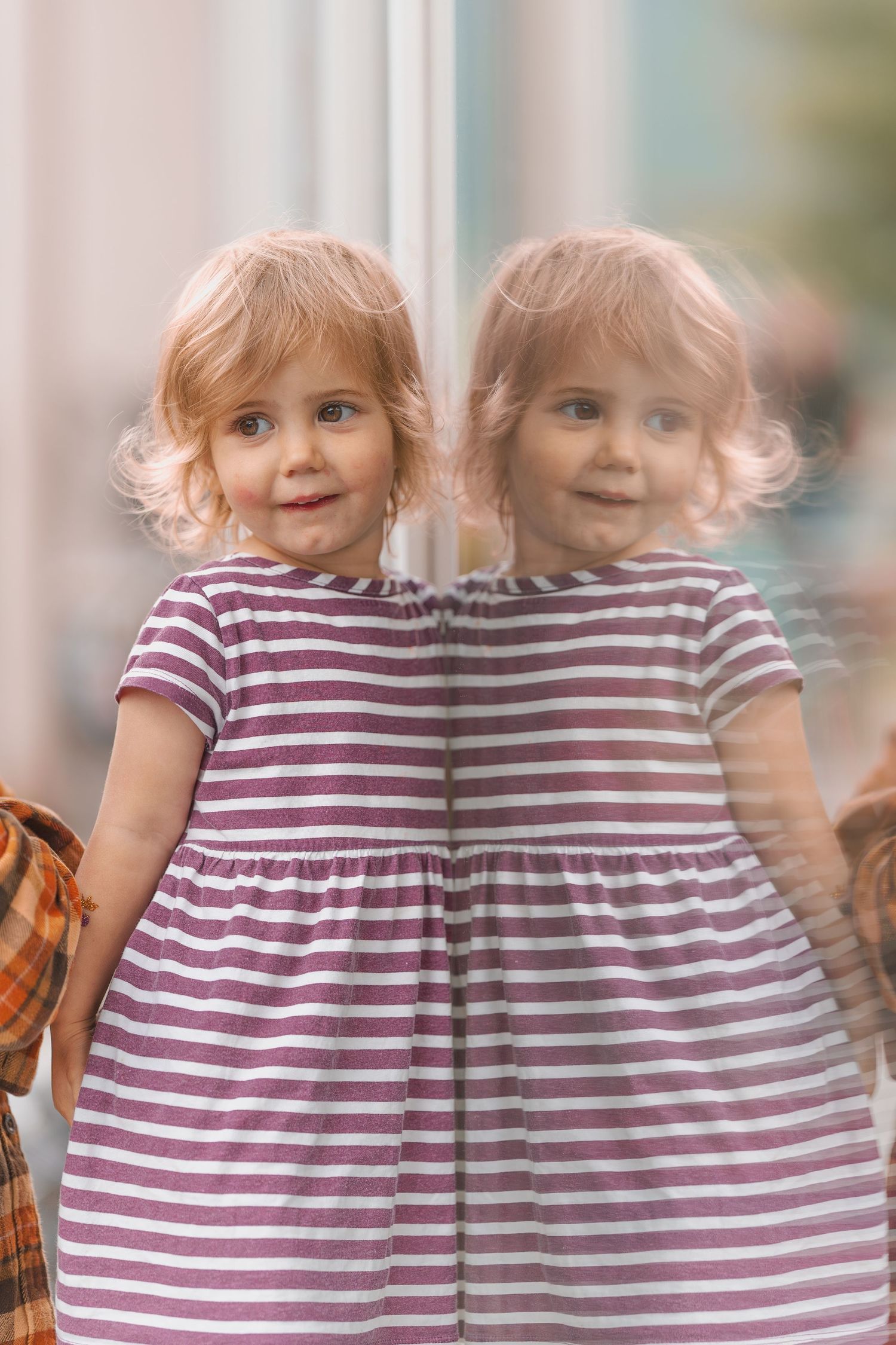 Two identical twins in striped dresses stand together.